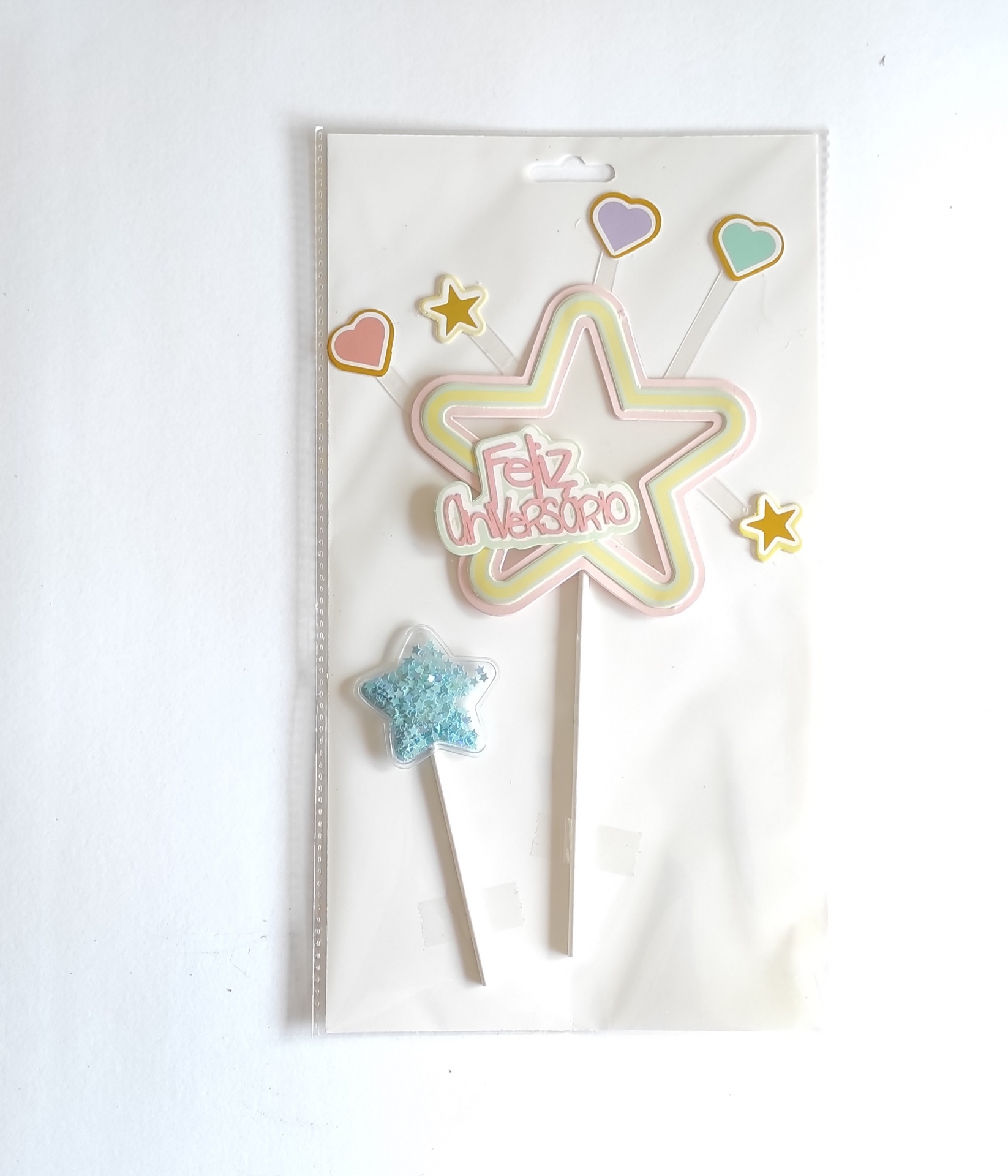 Decoração de bolo com estrela e texto 'Feliz Aniversário' em cores pastel e acessórios coloridos.