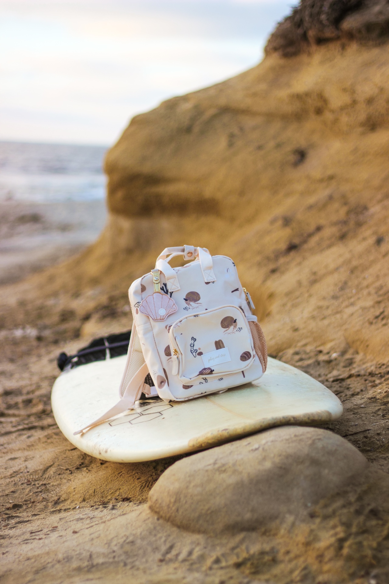 Mochila pequena cor-de-rosa com padrão sobre prancha de surf na areia junto ao mar