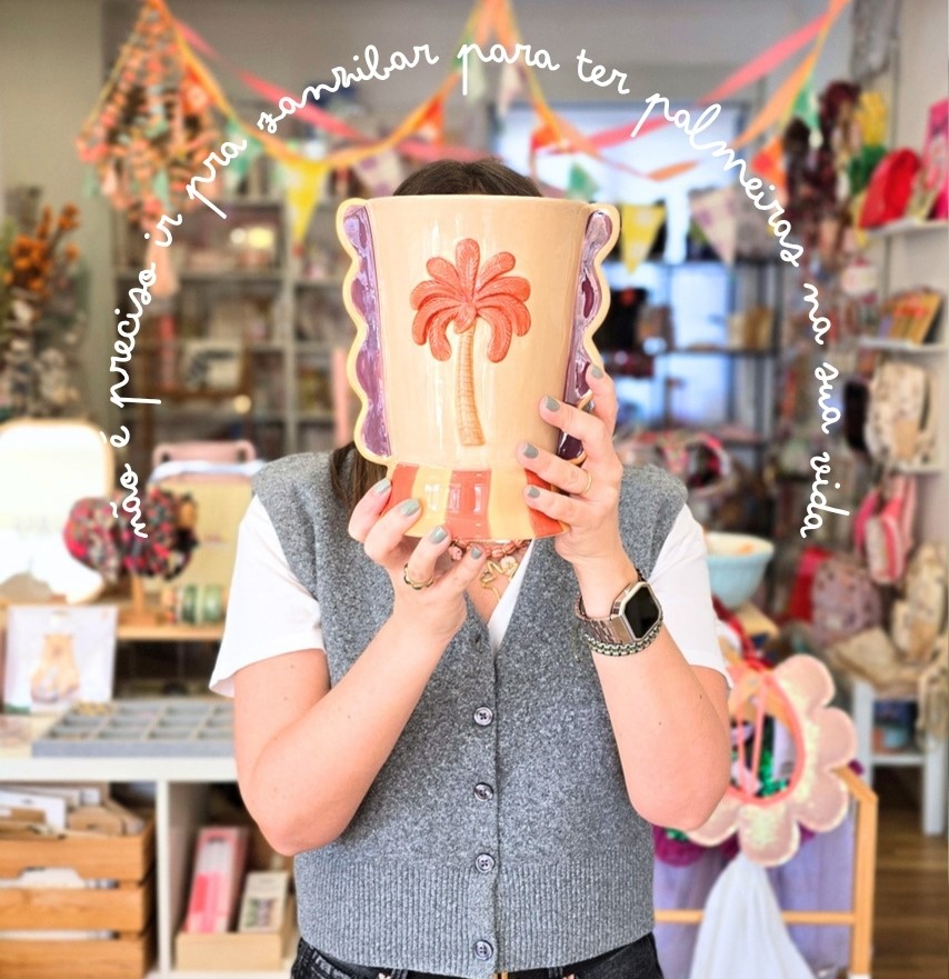 Vaso cerâmico colorido com desenho de palmeira segurado por pessoa em loja