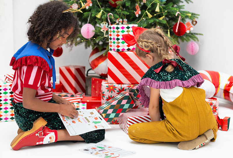 Duas meninas sentadas no chão perto da árvore de Natal com presentes coloridos