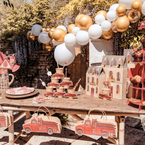 Mesa decorada para festa infantil com carrinhos de bombeiro em papel e balões brancos e dourados