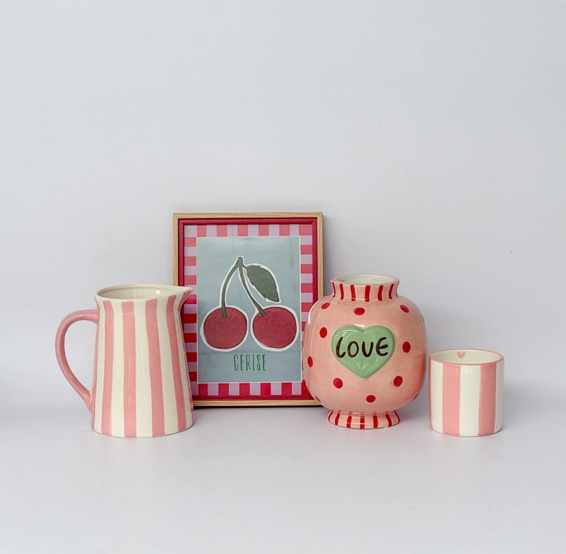 Conjunto decorativo com jarra, quadro de cerejas, vaso e copo com tons rosa e branco