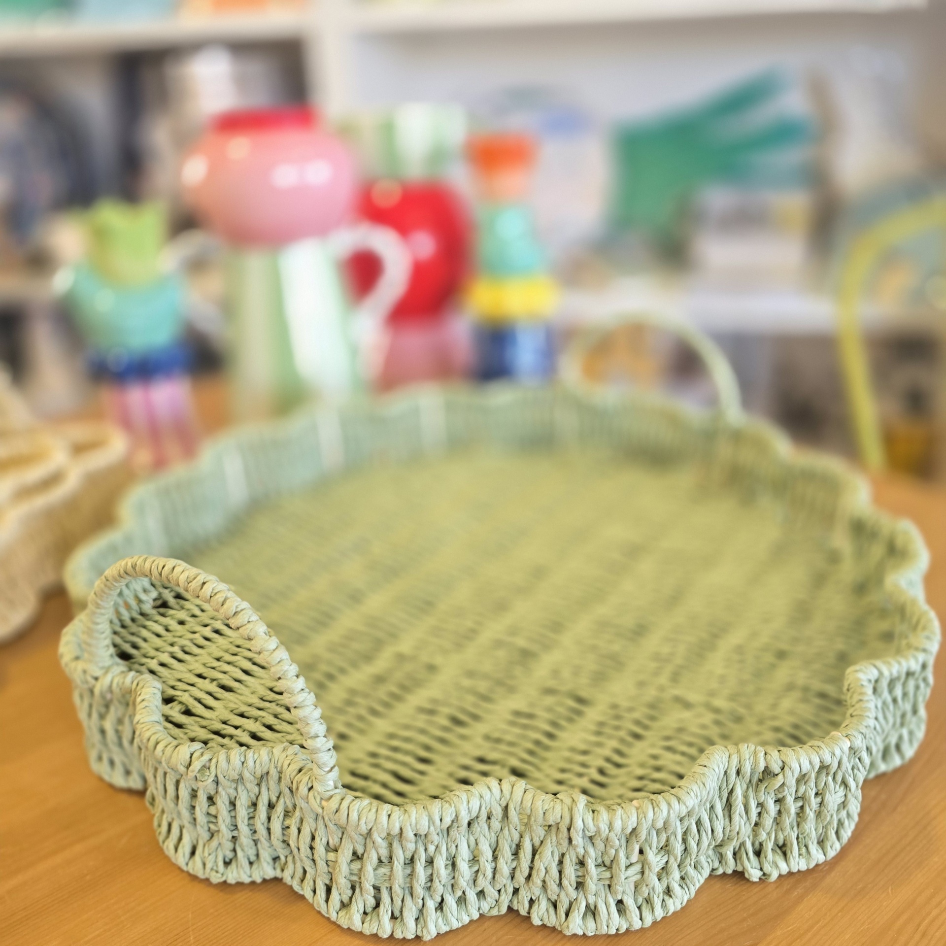 Tabuleiro oval de verga verde claro com borda ondulada e alças em mesa de madeira