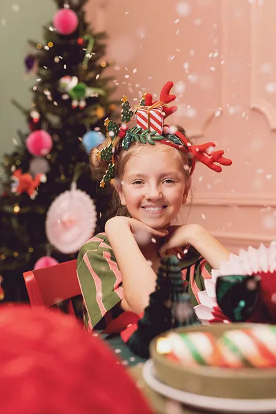 Menina com faixa de cabelo natalícia sorrindo sentada à mesa decorada para o Natal