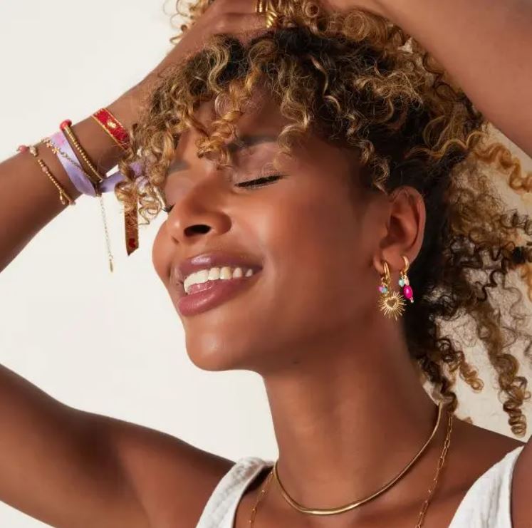 mulher sorrindo com brincos, colar e braceletes dourados e vermelhos