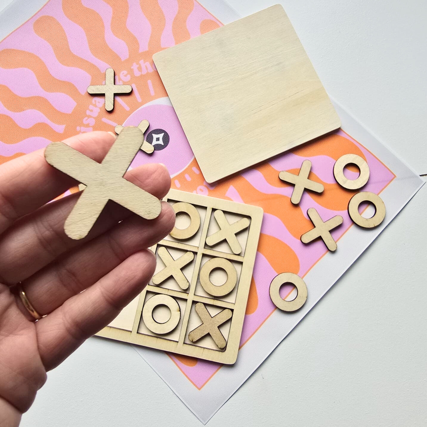 Jogo da velha em madeira com peças X e O sobre tabuleiro e tecido colorido