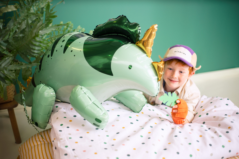 Balão de dinossauro verde e criança num quarto com cama e plantas