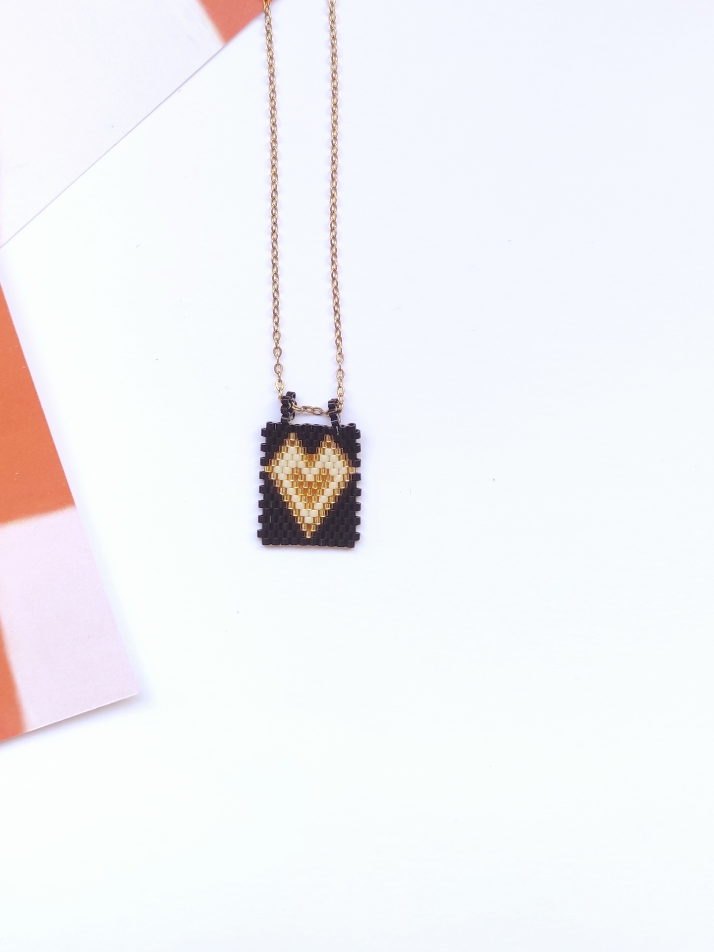 Colar com pendente retangular em padrão de coração em contas pretas, bege e amarelas com corrente dourada