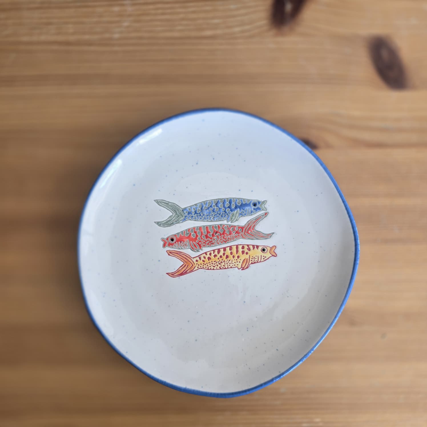 Prato de cerâmica branca com borda azul e decoração de peixes coloridos.