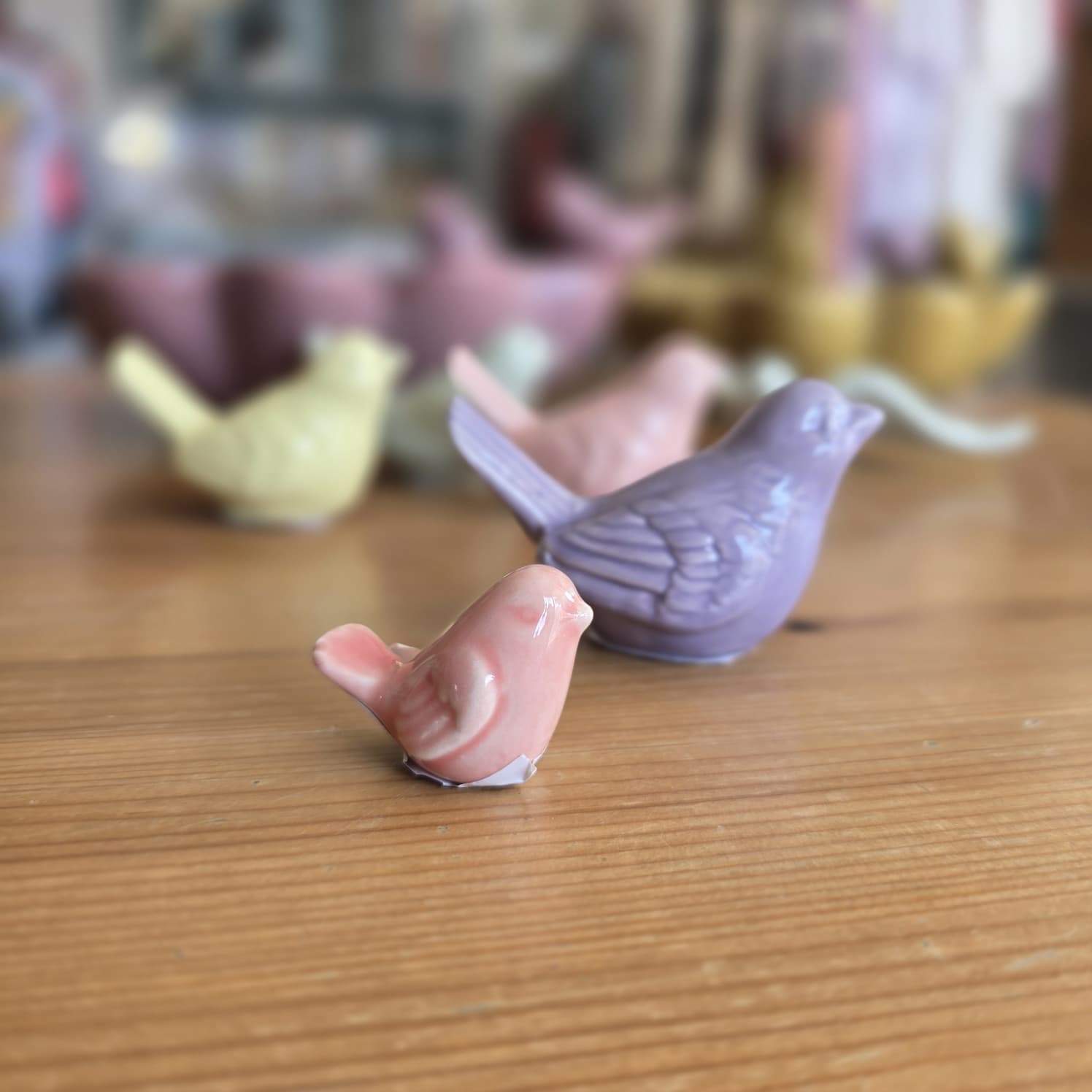 Figuras decorativas em cerâmica em forma de pássaros de várias cores pastel sobre mesa de madeira