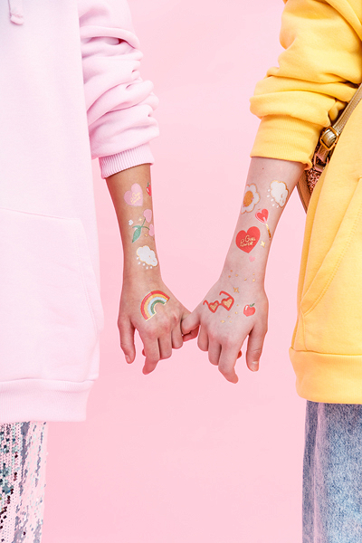 Braços com tatuagens temporárias coloridas e sweatshirts rosa e amarela segurando-se