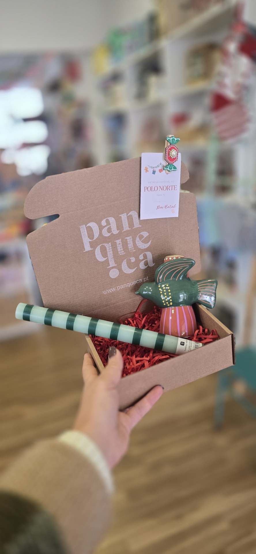 Caixa de cartão com ornamento de pássaro cerâmico e cilindro listrado, com etiqueta de entrega do Polo Norte.