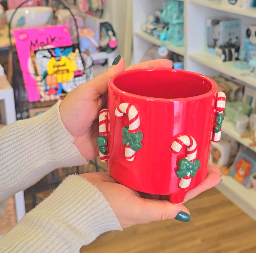 Caneca vermelha de cerâmica com bengalas de Natal em relevo segurada por mãos