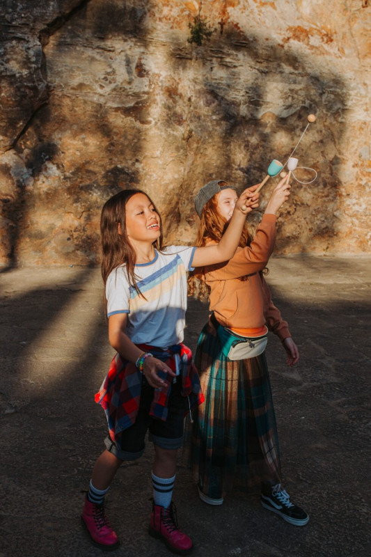 Duas crianças a brincar ao ar livre com brinquedos de madeira, parede de pedra ao fundo