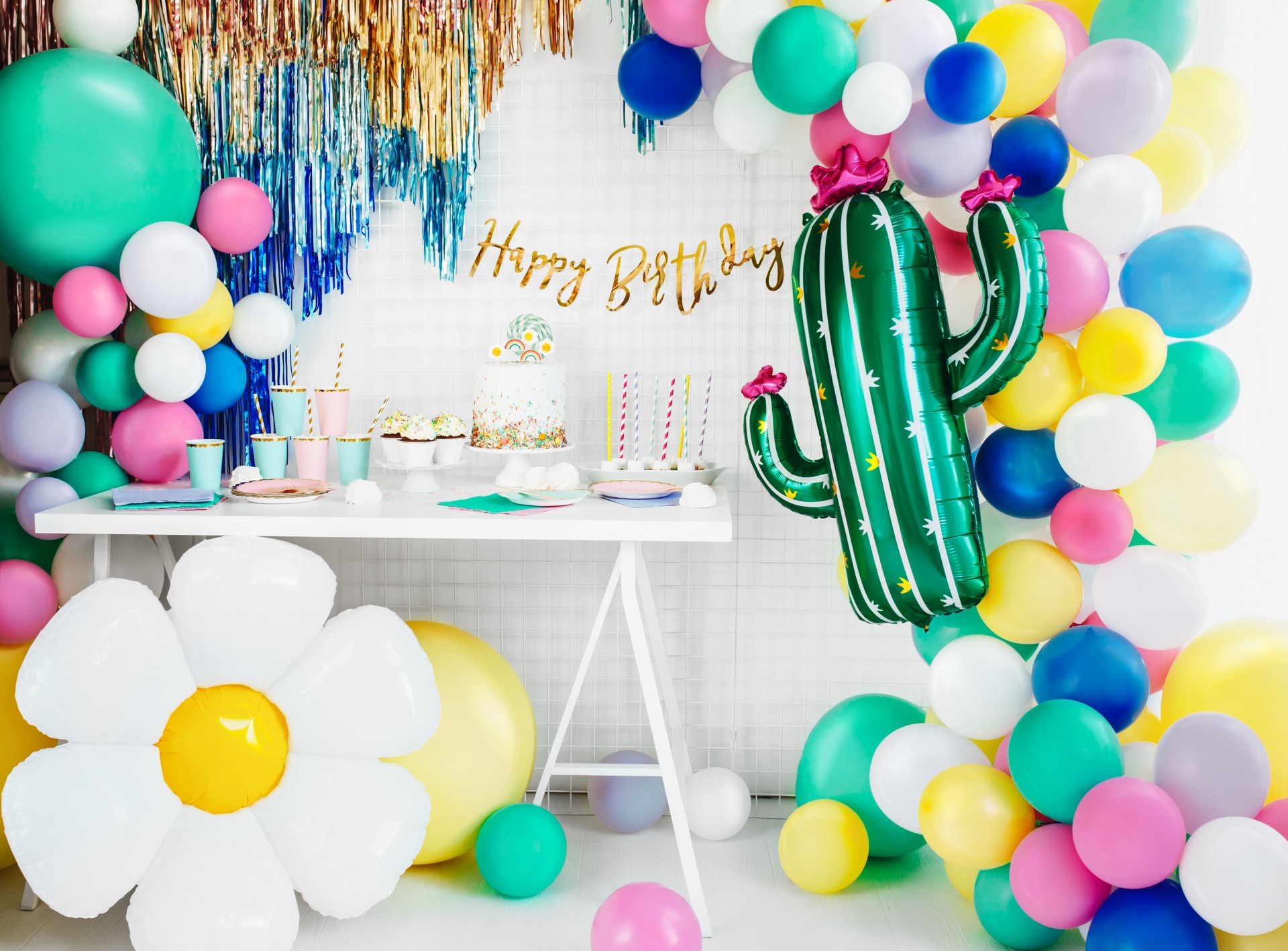 Decoração de festa de aniversário com balões coloridos e bolo numa mesa branca