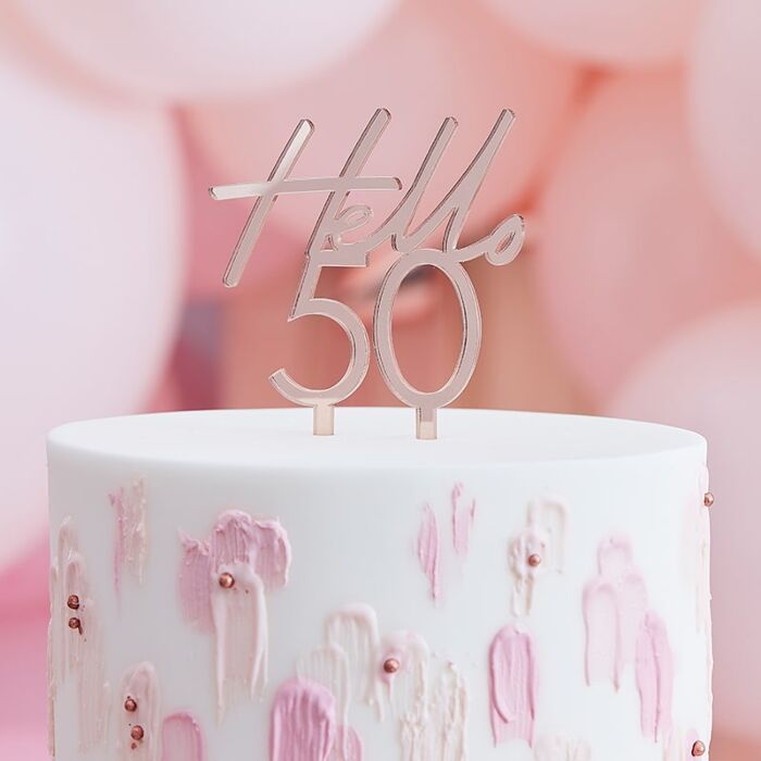 Bolo branco com decoração rosa e dourada e topo 'Hello 50'.