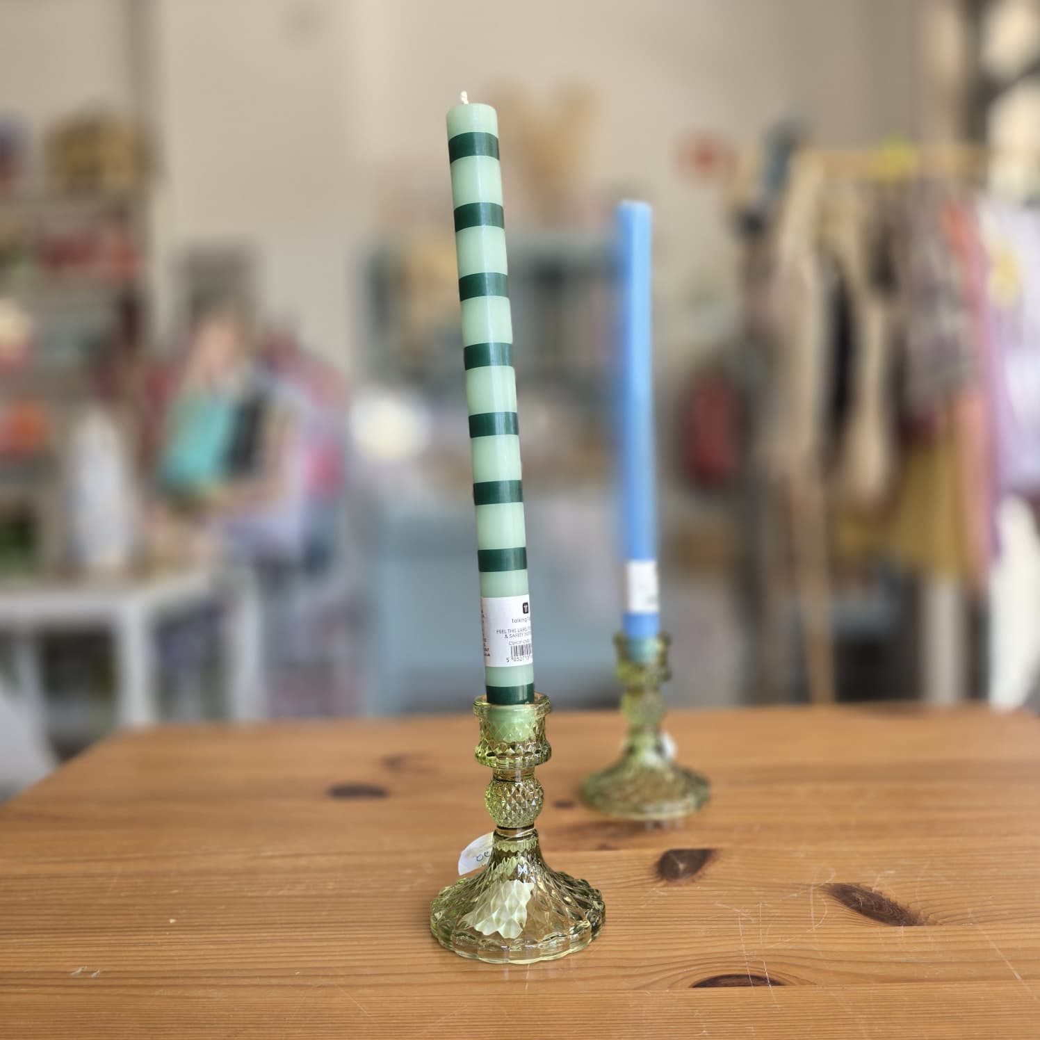 Duas velas altas em castiçais verdes com textura facetada sobre uma mesa de madeira em loja