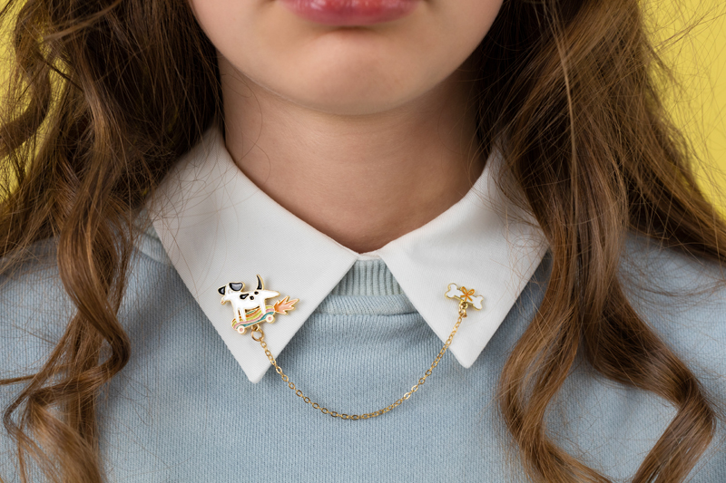 colar de gola com brosches de vaca e flor ligados por corrente em camisa azul clara com gola branca