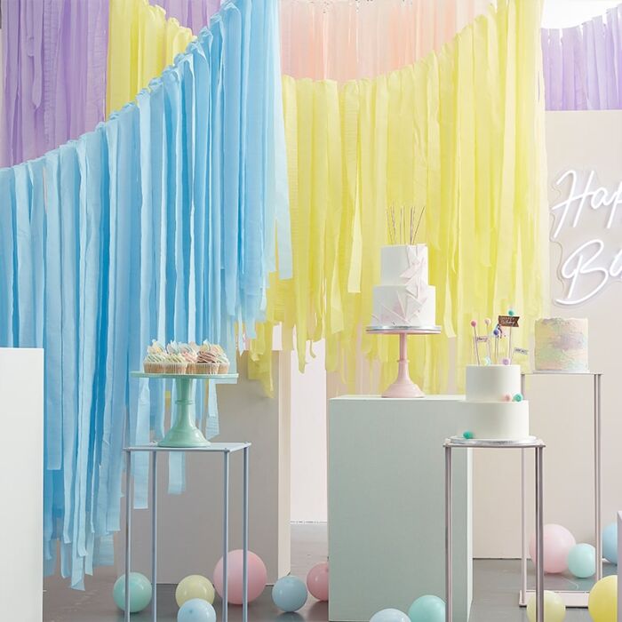 Mesa com bolos decorados, franjas de papel coloridas e balões num ambiente festivo