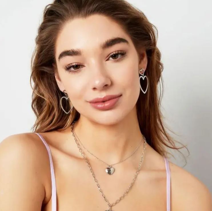 Mulher com brincos e colares prateados com corações, esfera e cruz