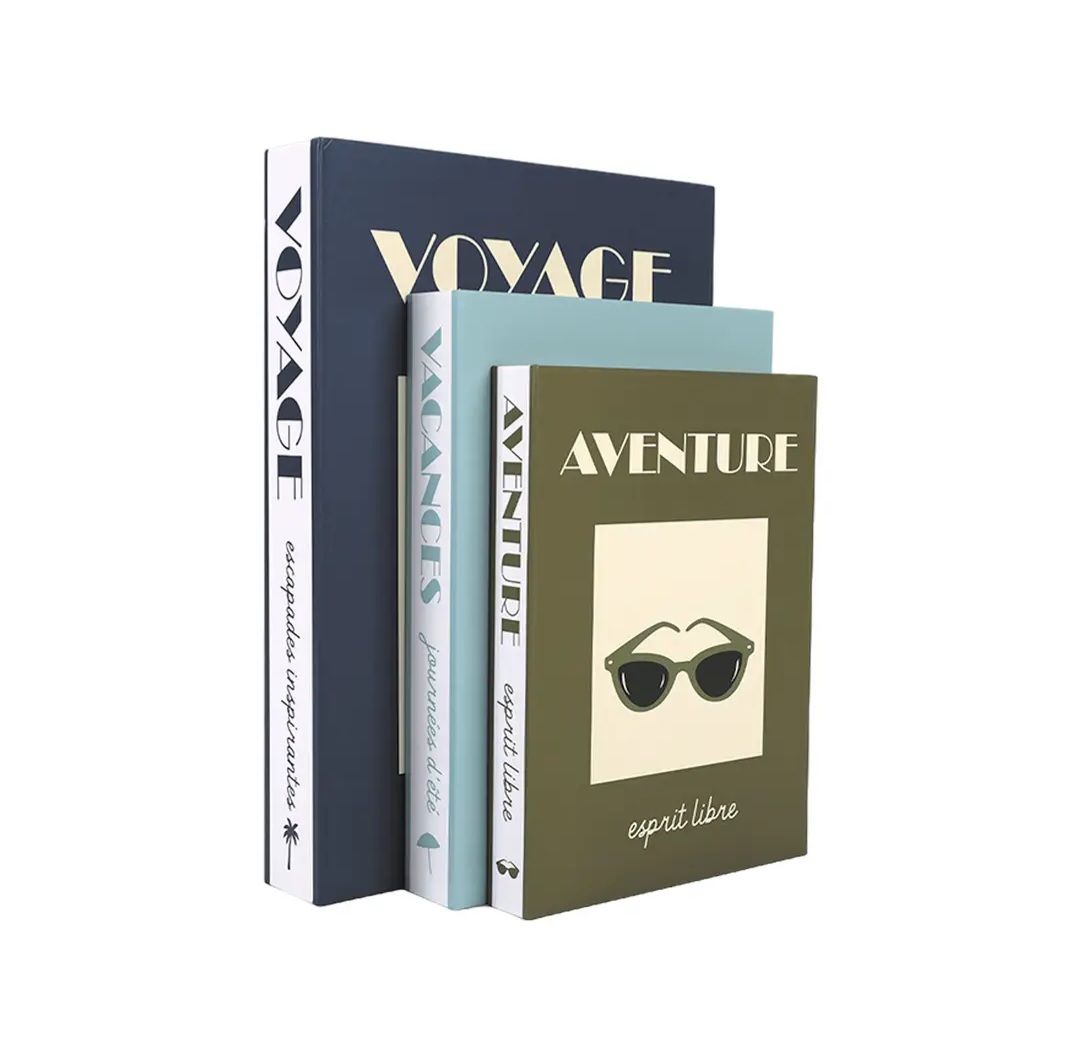 Três livros decorativos empilhados com capas azul escuro, azul claro e verde-oliva e texto em francês.