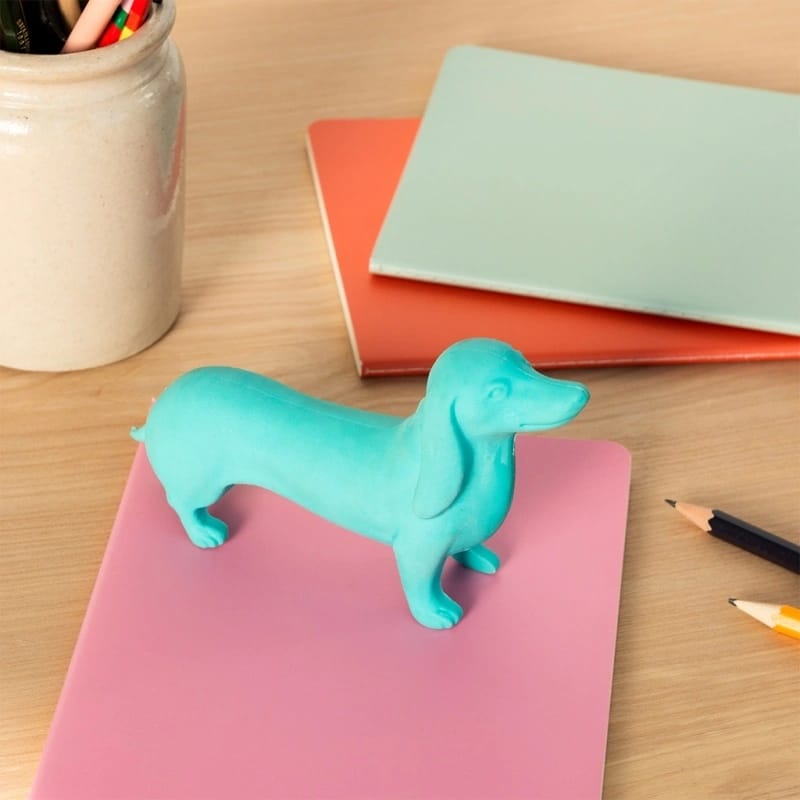 Estatueta azul de cão Dachshund sobre pasta rosa em mesa com pastas coloridas e lápis