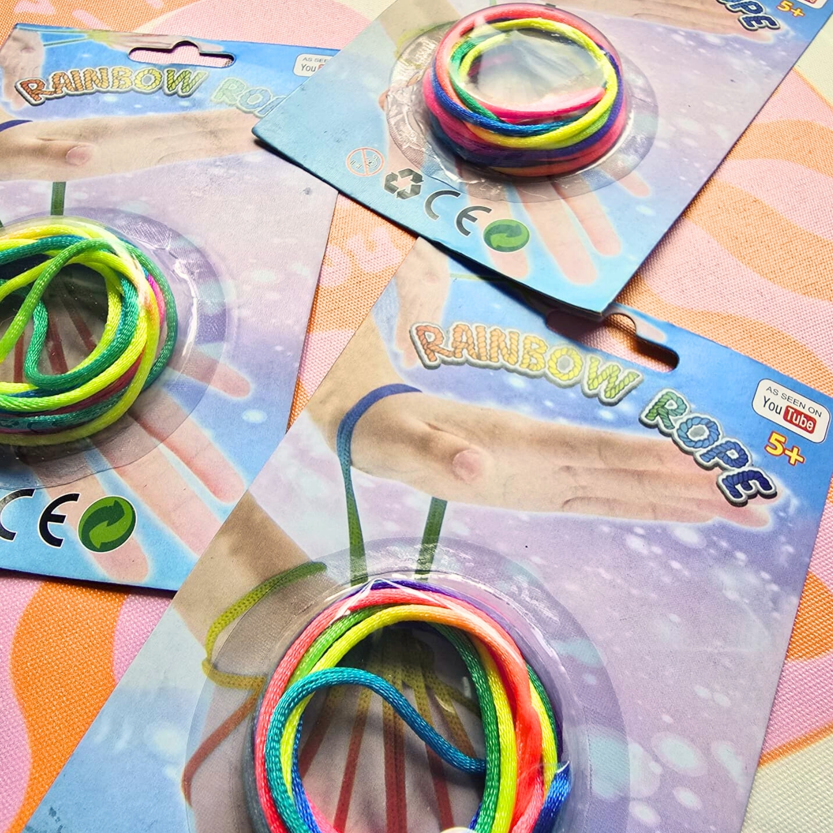 Brinquedo Rainbow Rope em pacotes com cordas coloridas arco-íris e fundo cor-de-rosa.