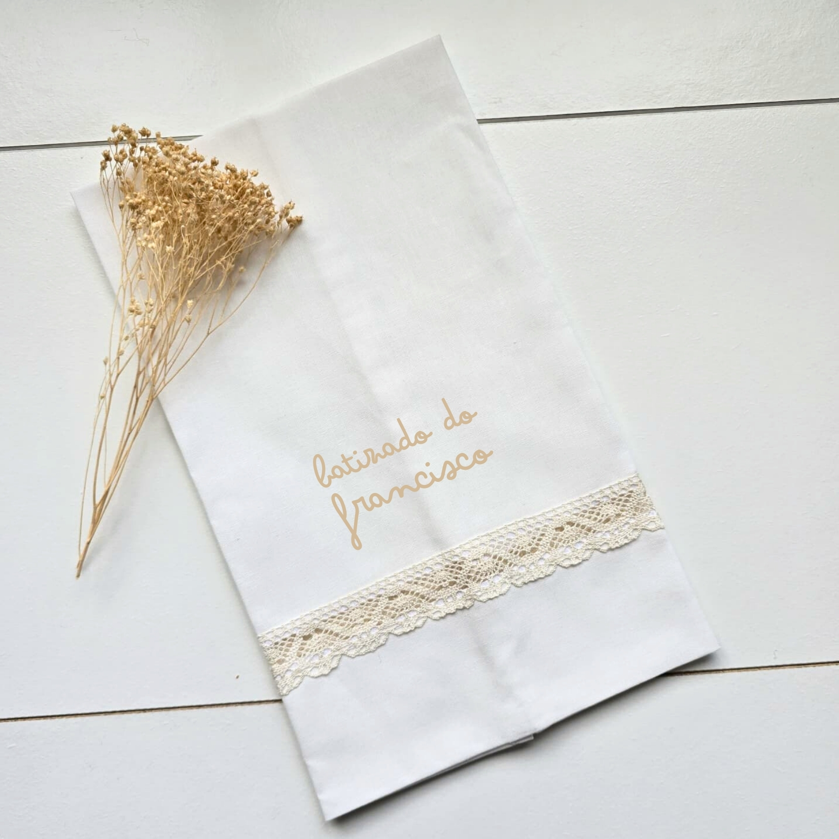 Toalha branca com bordado bege e renda, e ramo seco ao lado