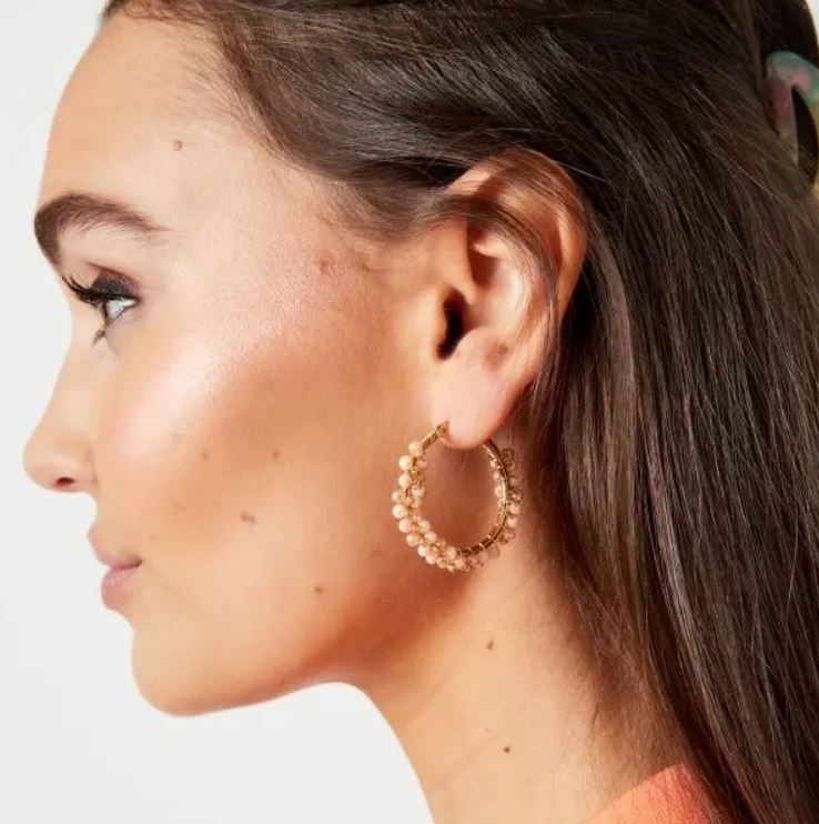 Brincos de argola dourados com pérolas numa mulher com cabelo castanho escuro.