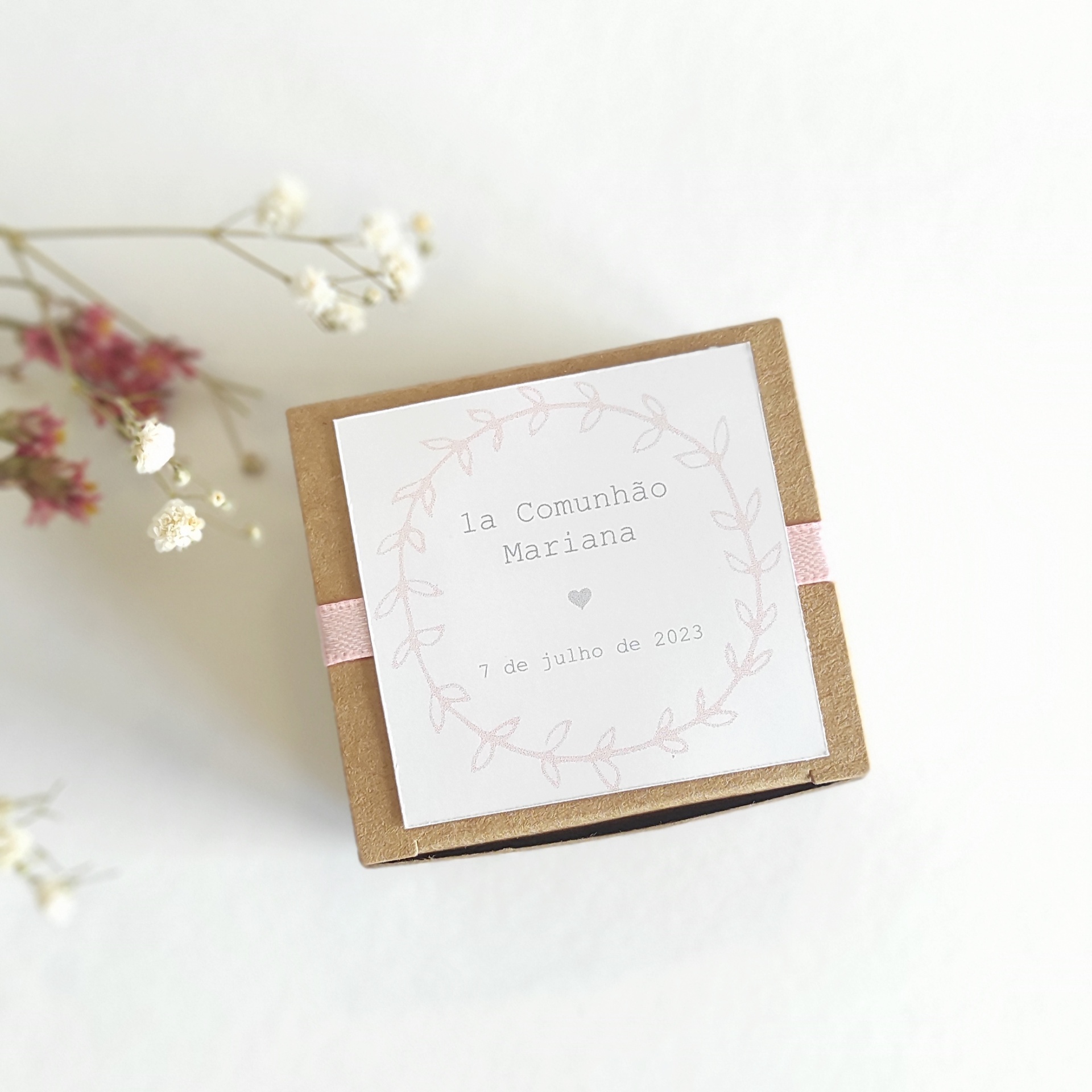 Caixa pequena de papel castanho com etiqueta branca e fita cor-de-rosa