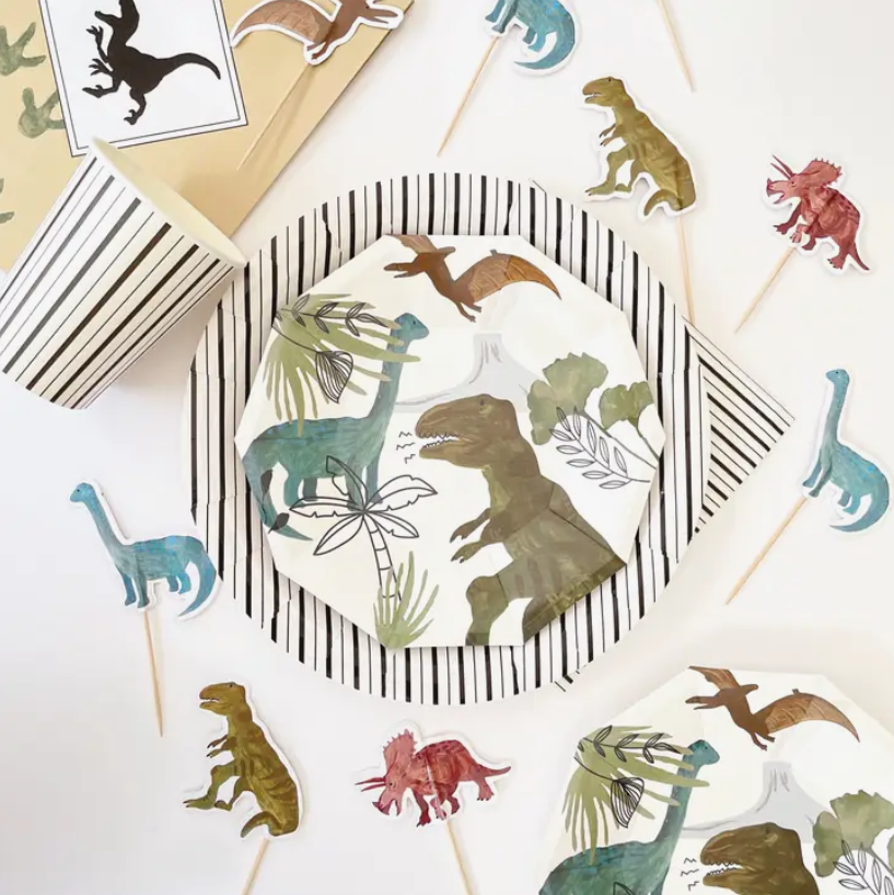 Conjunto de festa infantil com tema de dinossauros, pratos e copos de papel, palitos decorativos e saco de papel listrado.