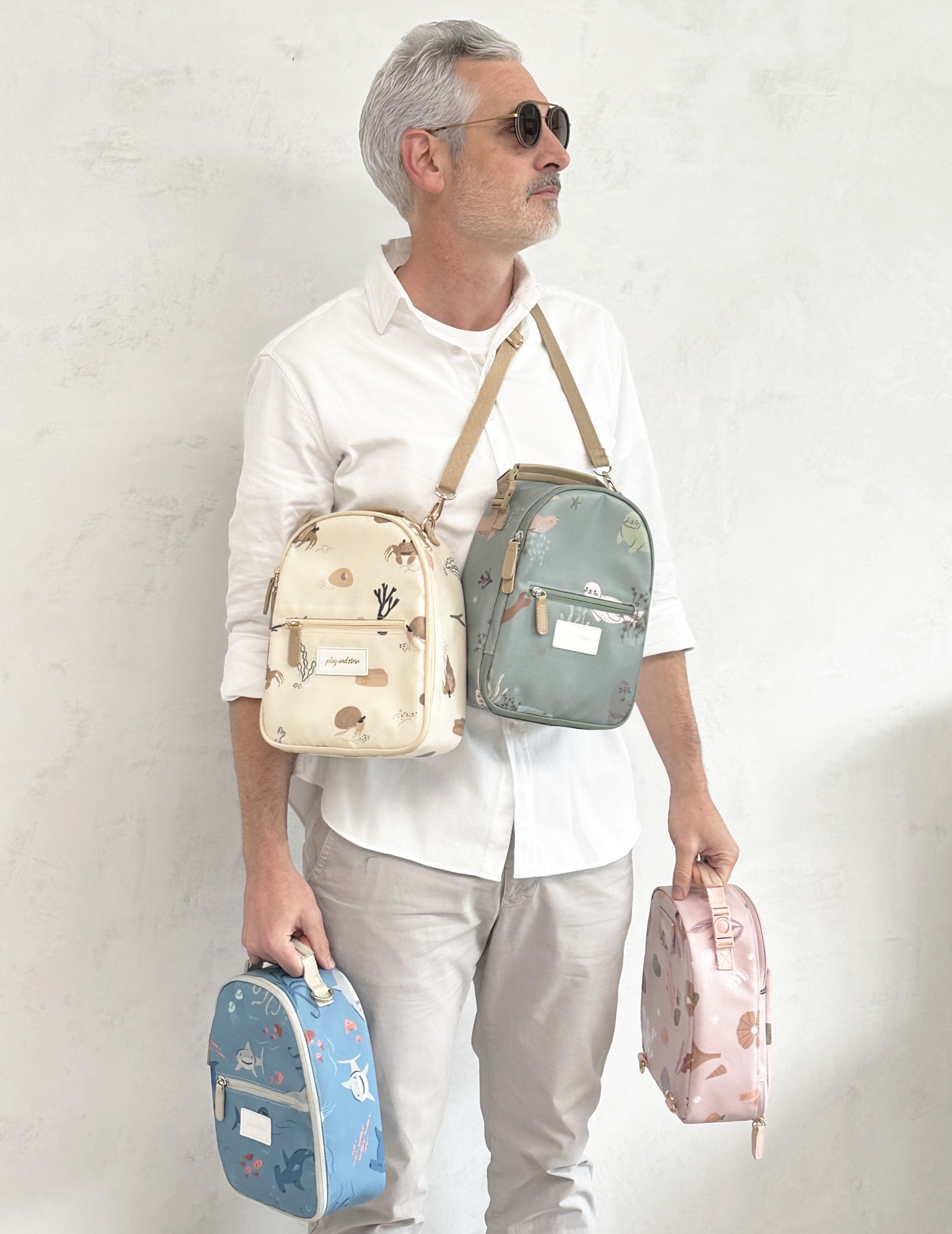 Homem com quatro mochilas pequenas de diferentes cores com padrões de cogumelos