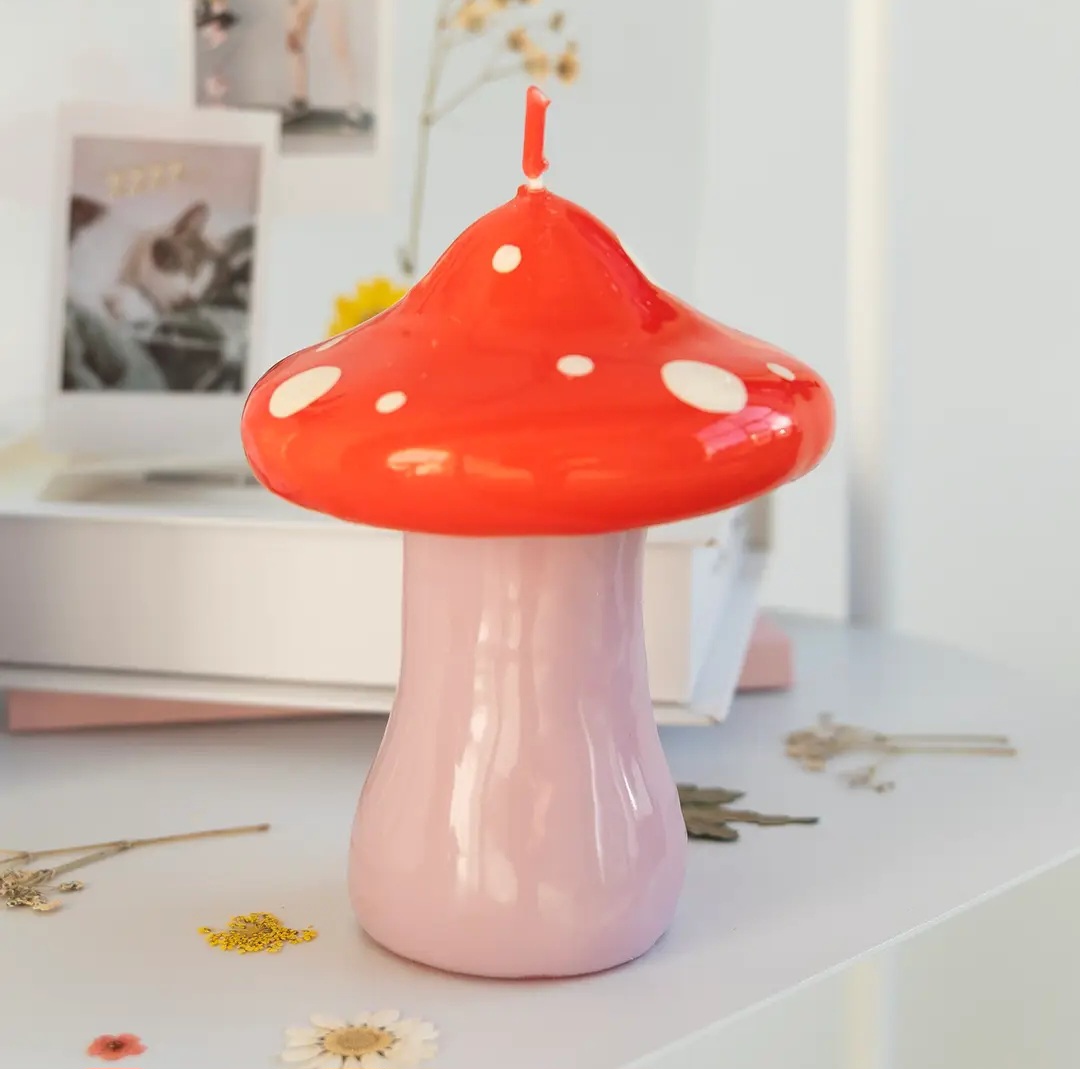 Vela em forma de cogumelo vermelha e rosa com pintas brancas numa mesa branca