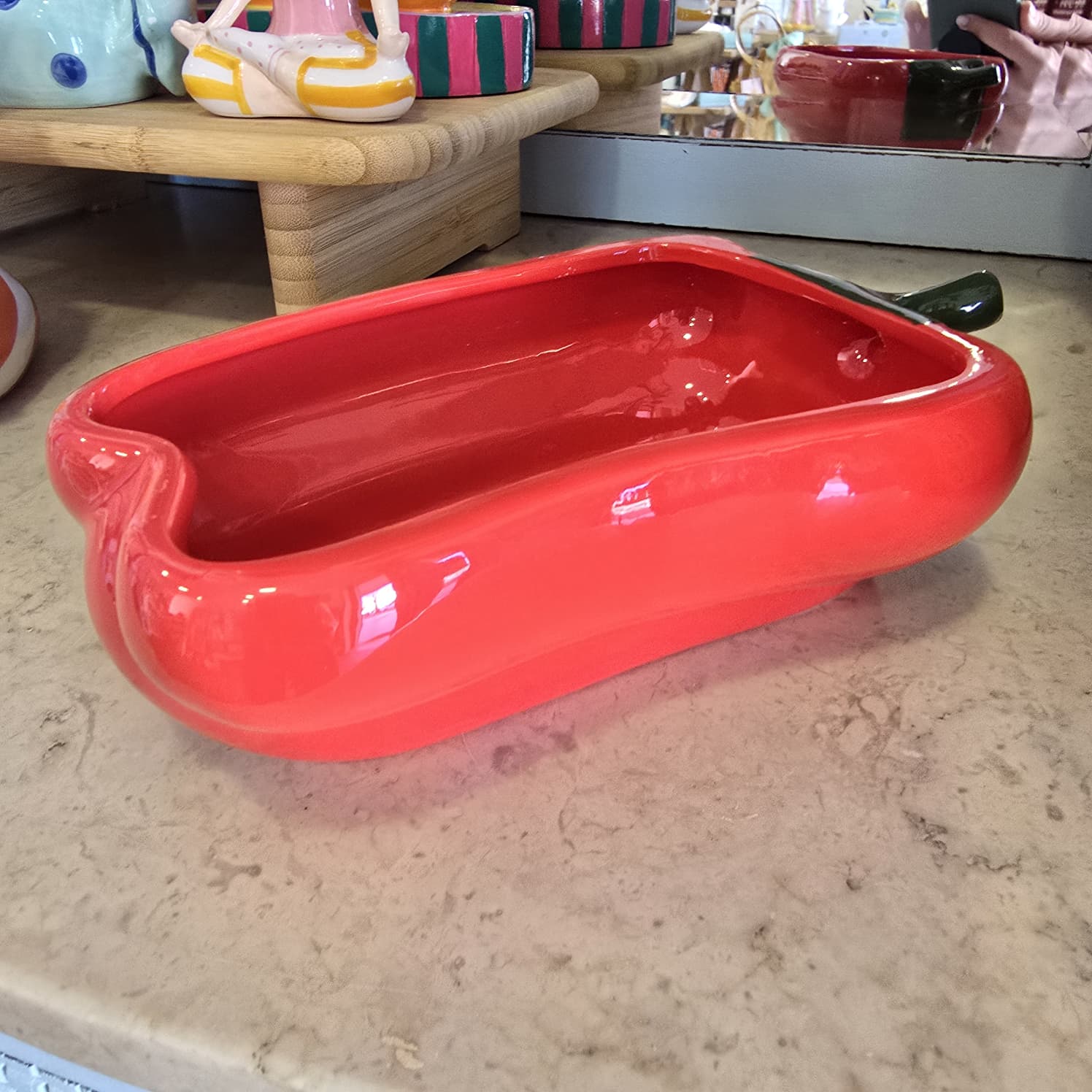 Tabuleiro cerâmico vermelho em forma de pimento com caule verde.