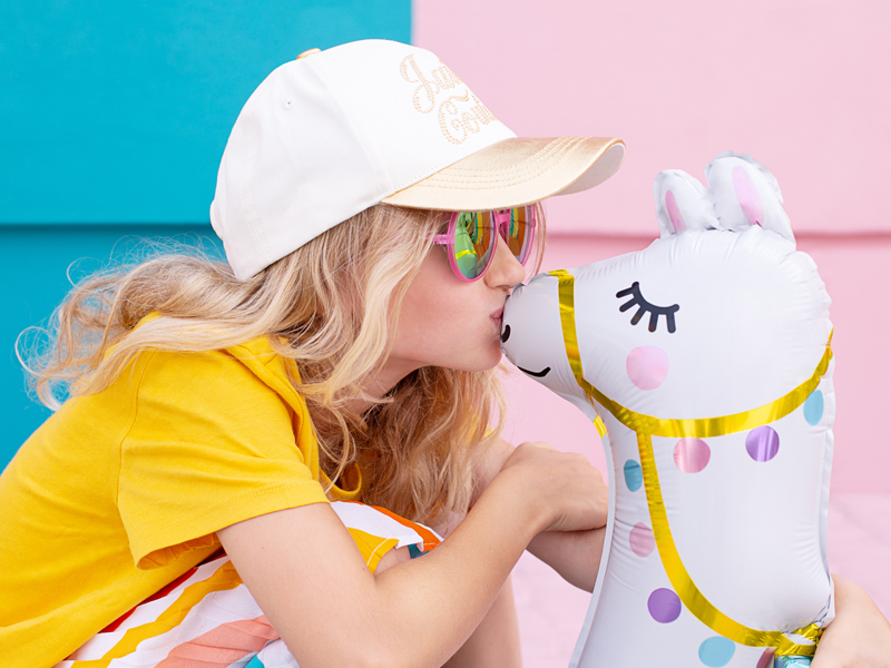 Criança loira a beijar balão insuflável em forma de lhama colorida