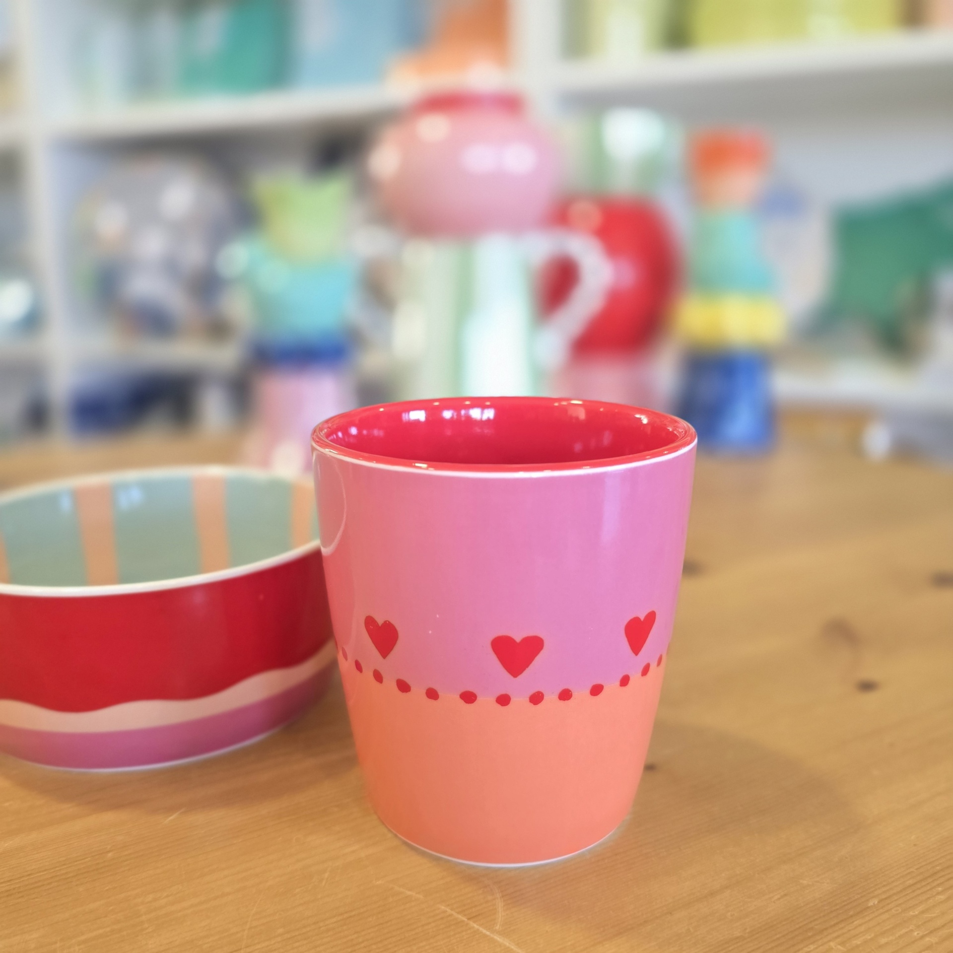 Caneca rosa e vermelha com corações sobre mesa de madeira