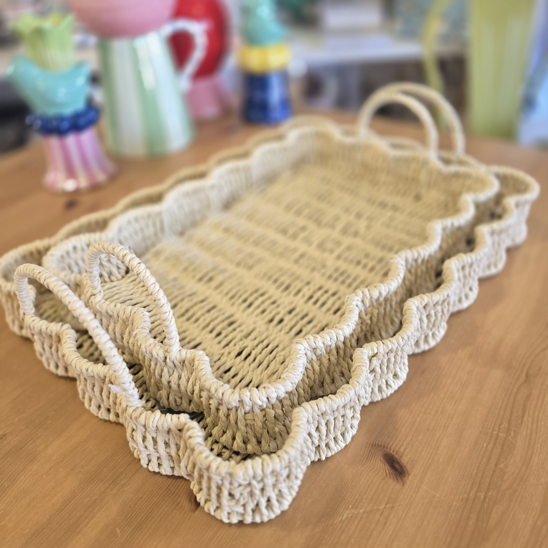 Bandejas entrelaçadas de material trançado cor bege com bordas onduladas e alças sobre mesa de madeira