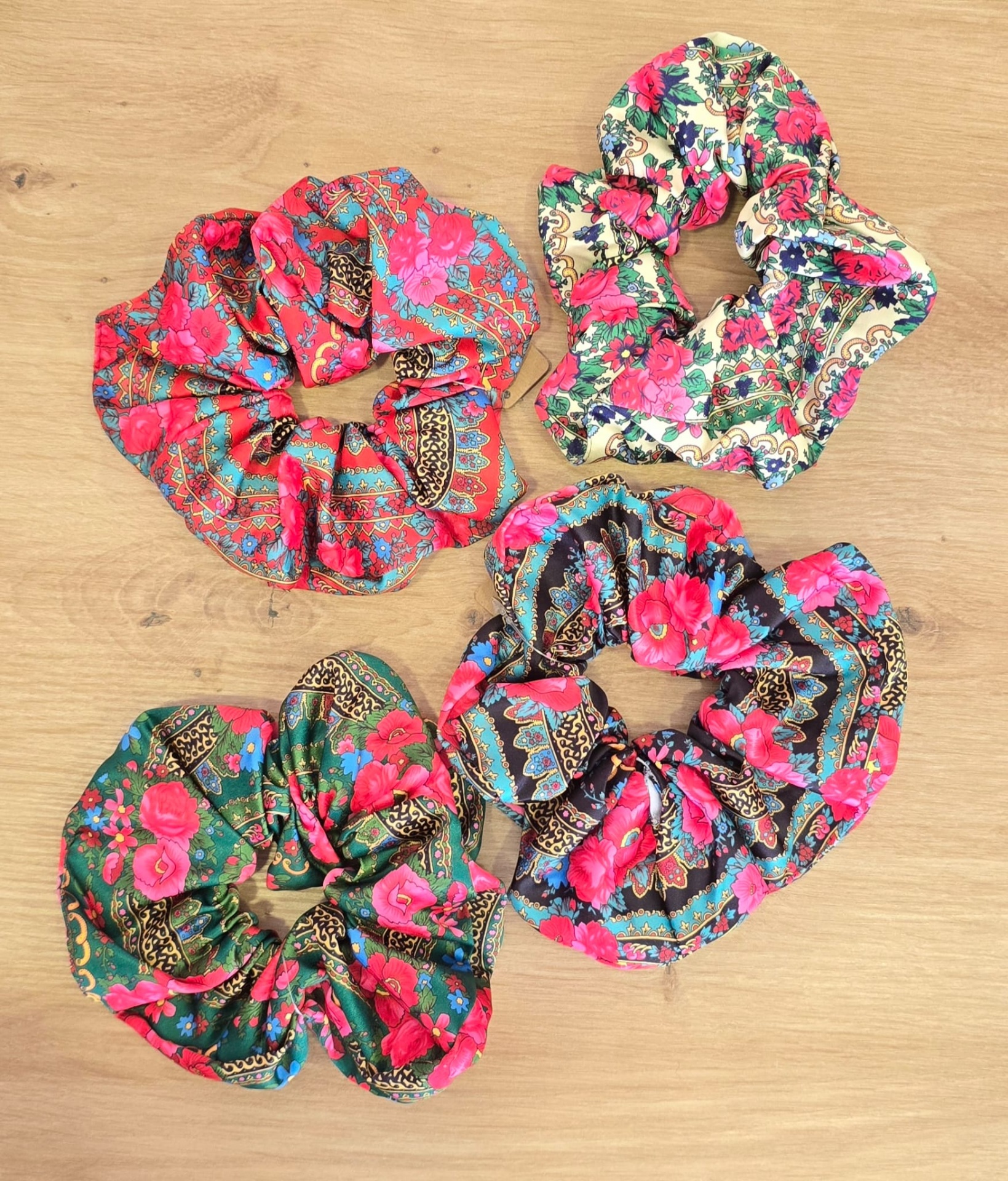 Quatro scrunchies florais coloridos sobre madeira clara.