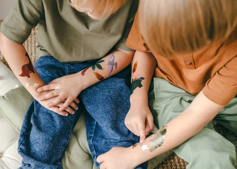 Duas crianças com tatuagens temporárias sentadas em superfície almofadada clara