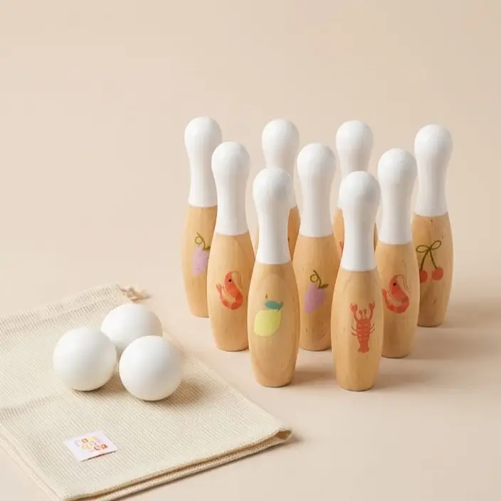 Conjunto de bowling infantil com pinos de madeira pintados e bolas brancas sobre saco de tecido.