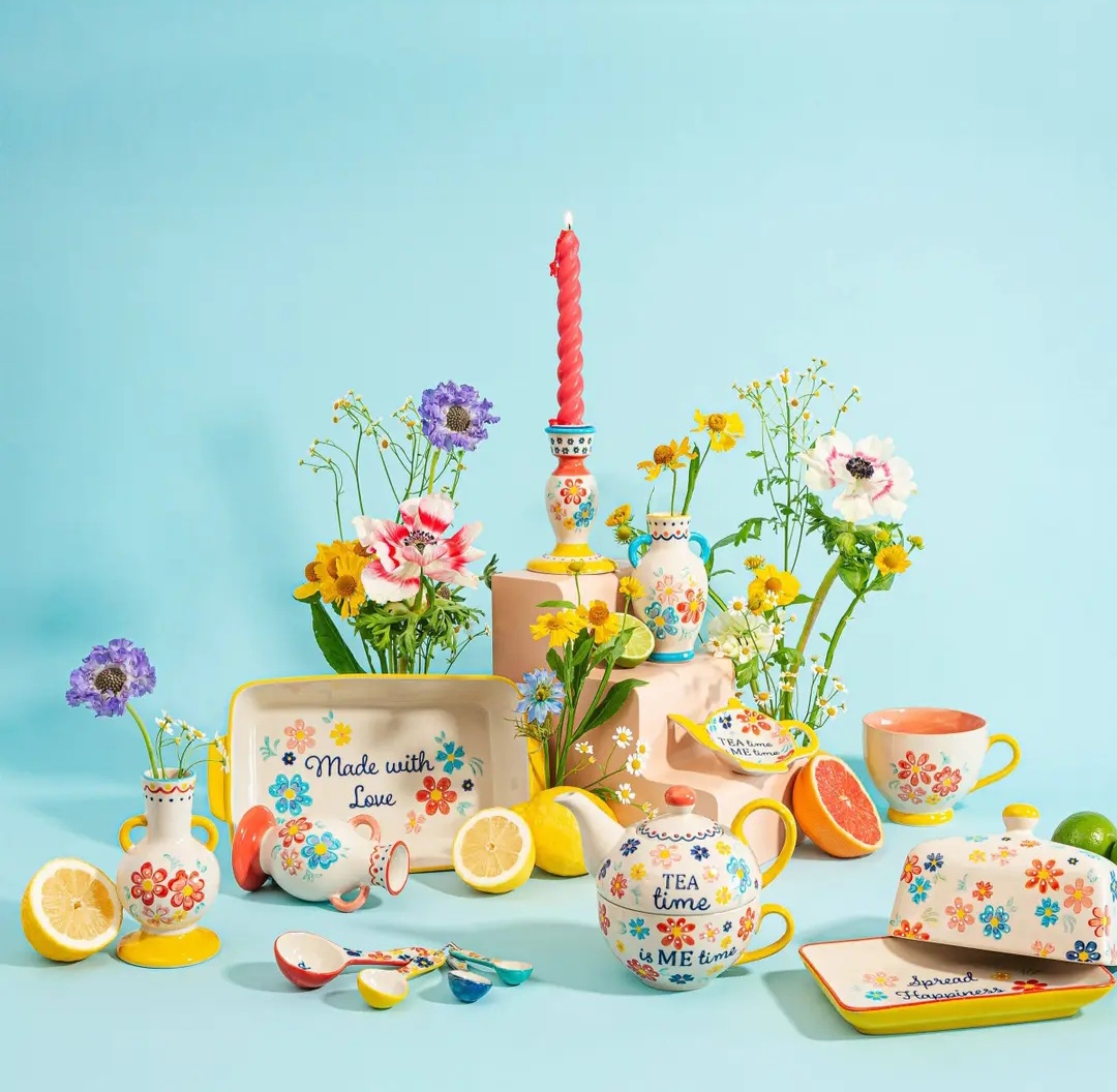 Conjunto de chá em cerâmica colorida com flores, vela vermelha, limões e flores em fundo azul.