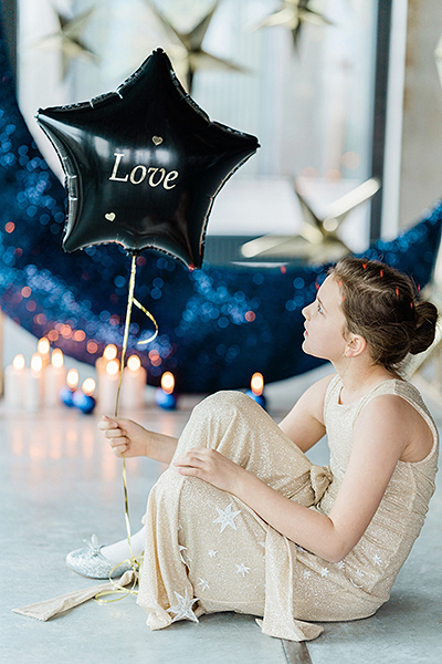 Menina sentada com vestido bege e balão preto estrela com texto 'Love'