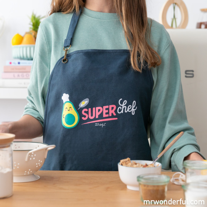Avental azul escuro com estampa de abacate e texto SUPER chef usado por pessoa em cozinha
