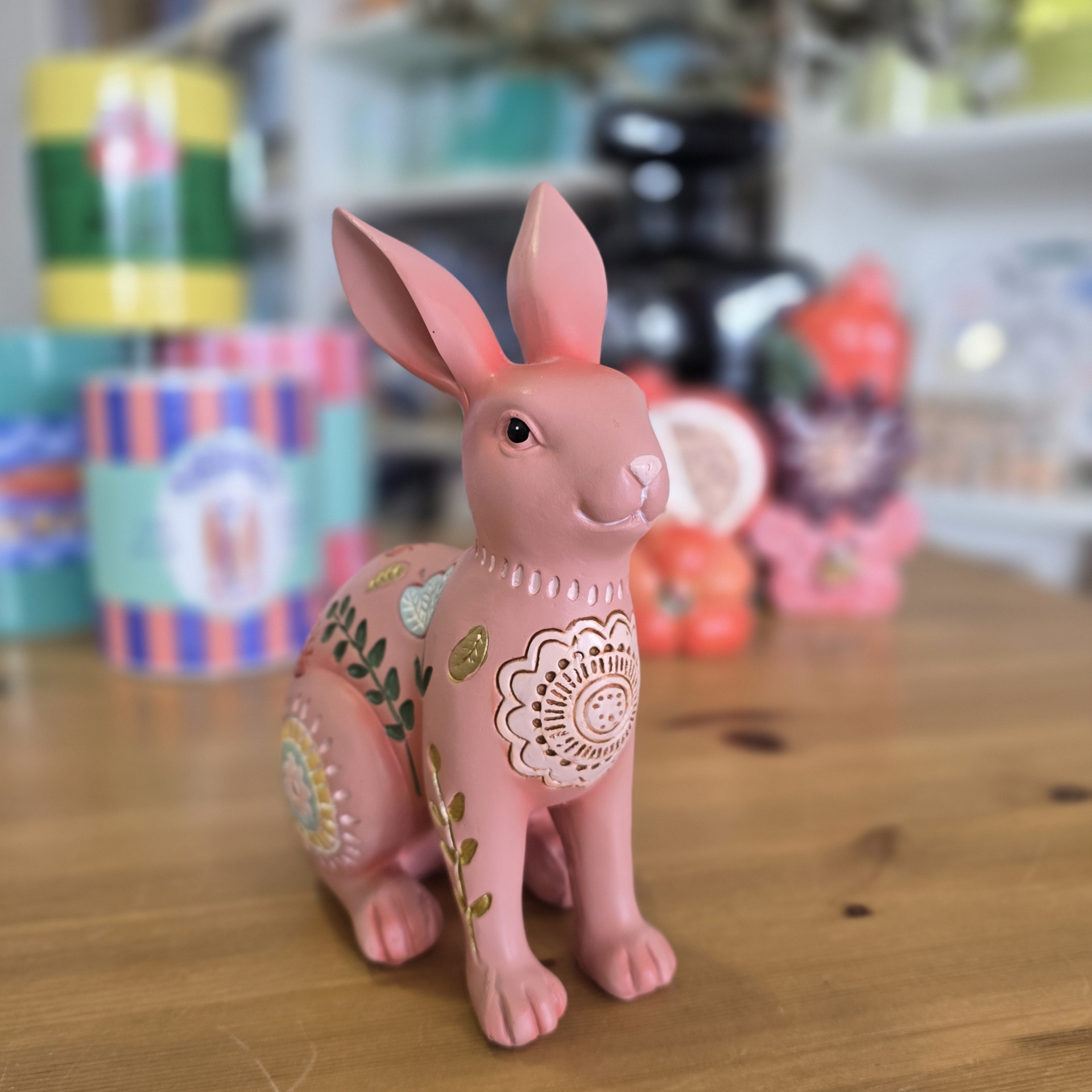 Estatueta de coelho rosa com padrões florais coloridos sobre mesa de madeira