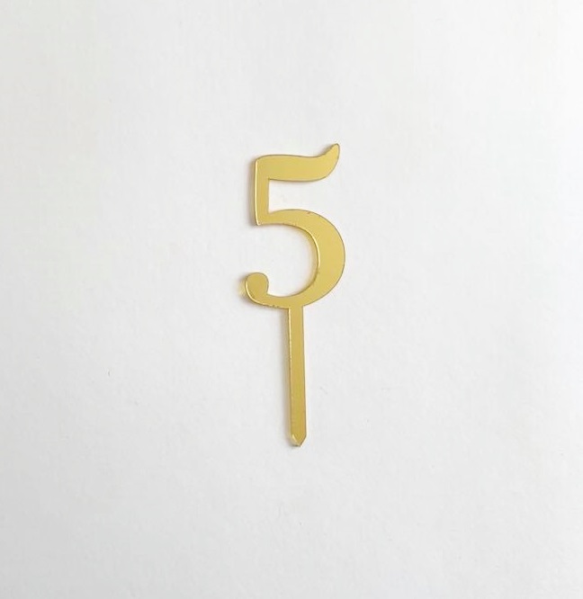 Número 5 dourado em metal com base fina sobre fundo branco