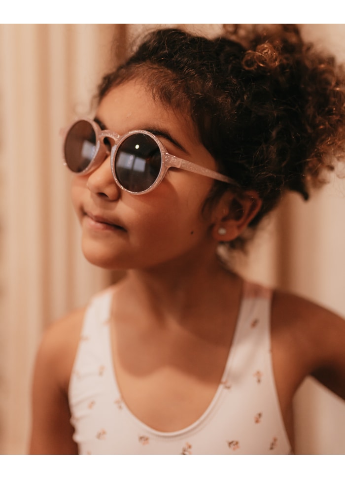 Criança com óculos de sol rosa e camisola branca com flores