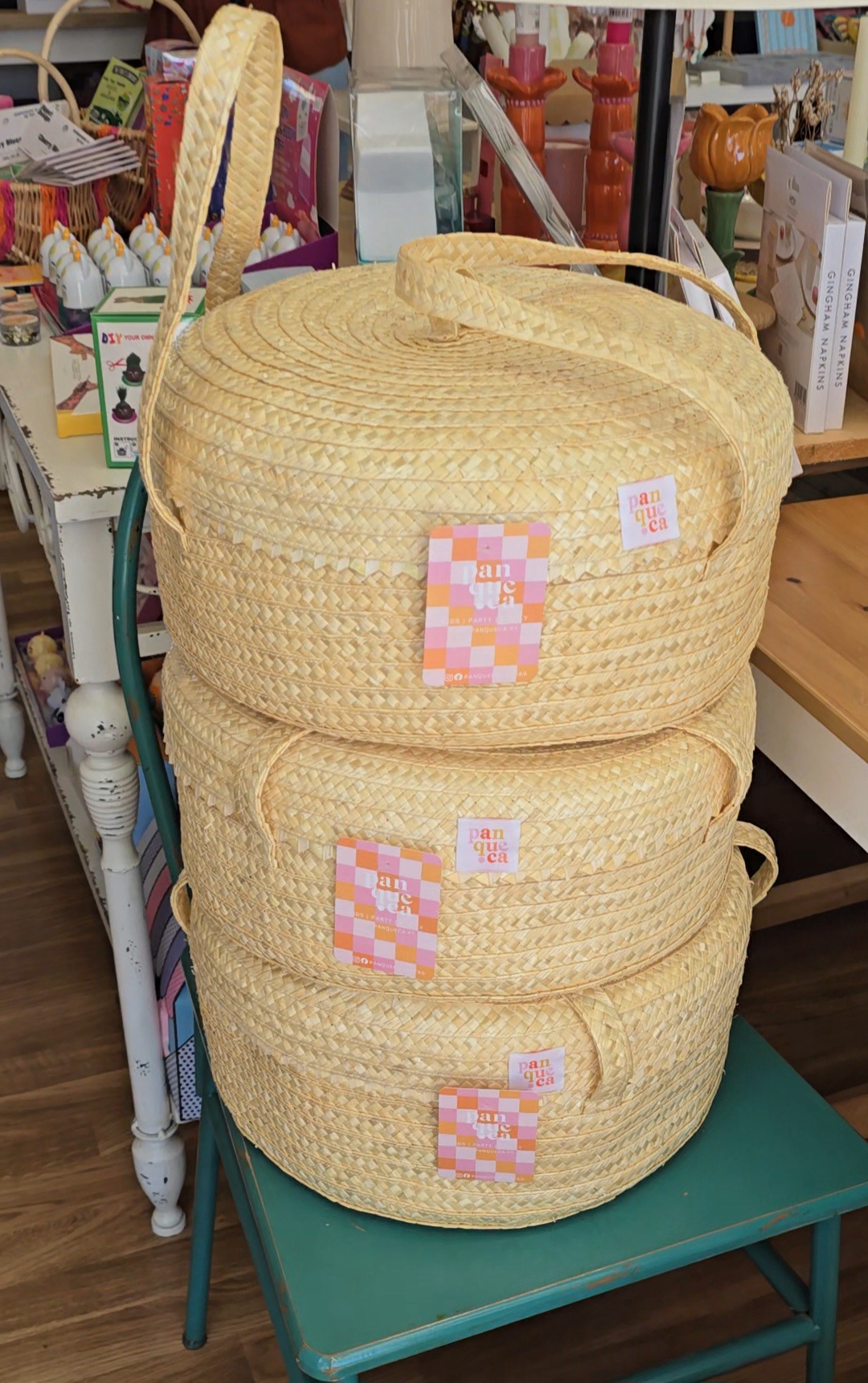 Três cestas de palha empilhadas numa cadeira verde numa loja.