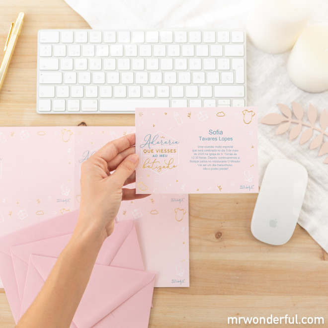 Cartão personalizado rosa com texto em português segurado à frente de teclado branco e objetos sobre uma mesa de madeira