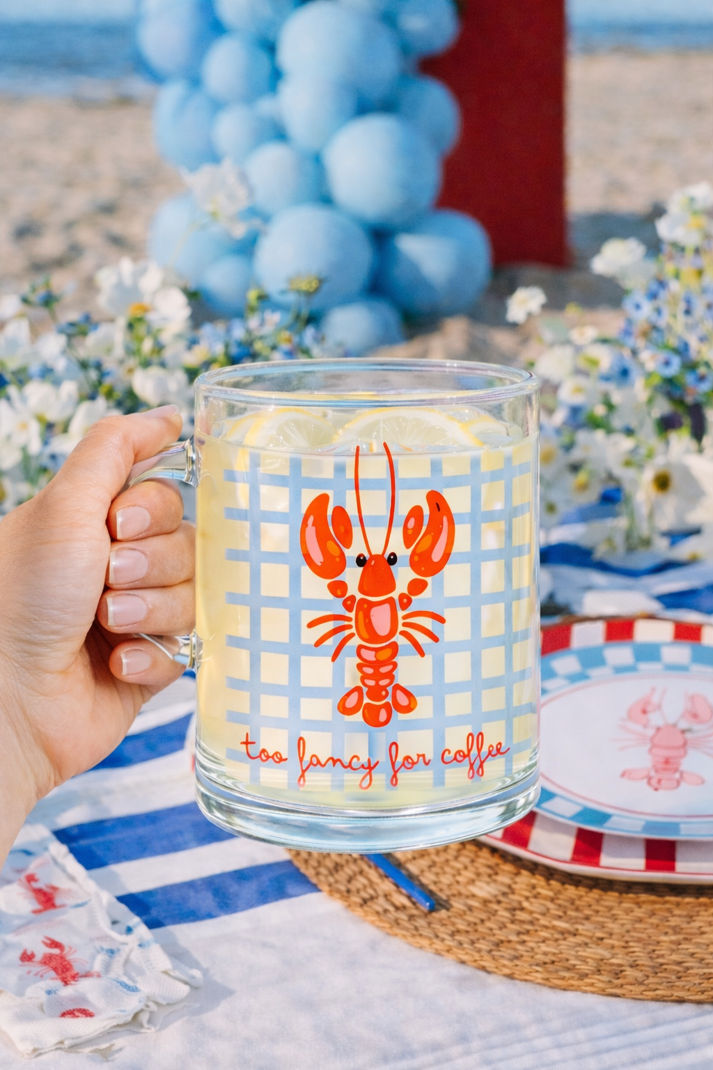 Caneca de vidro com lagosta e texto, contendo limonada, numa mesa decorada ao ar livre