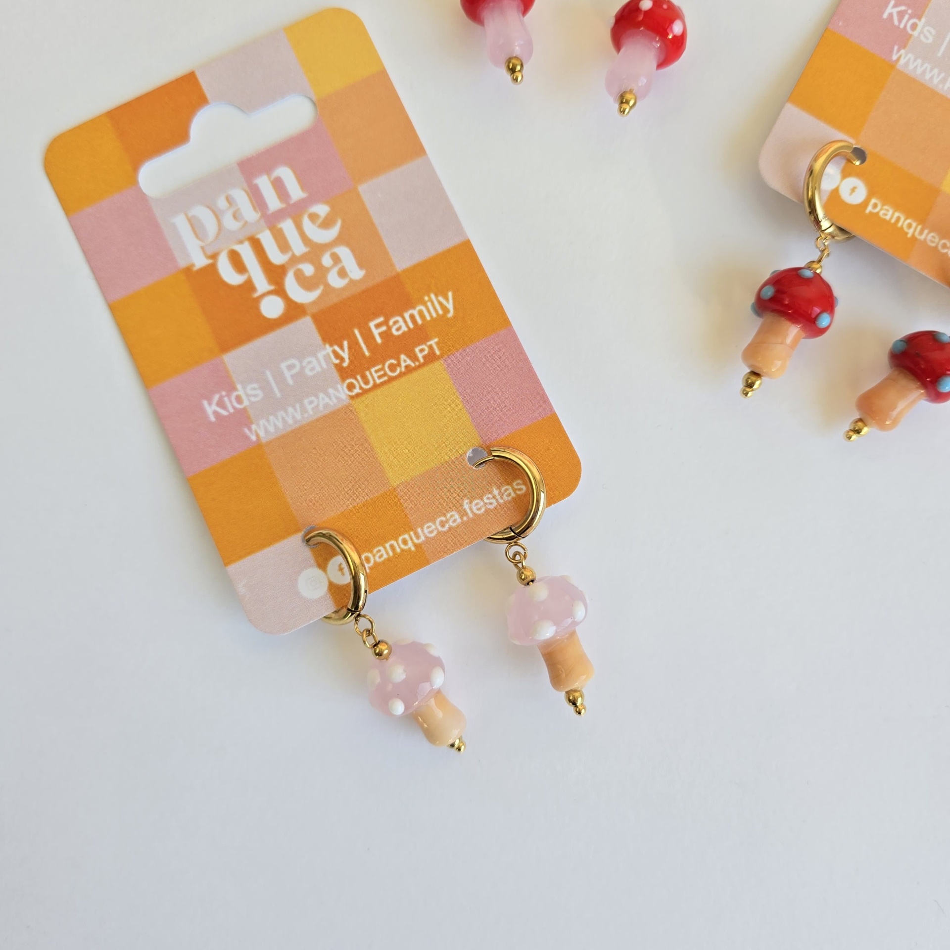 Brincos em forma de cogumelo cor-de-rosa com pintas brancas e cartolina com padrão quadriculado e texto
